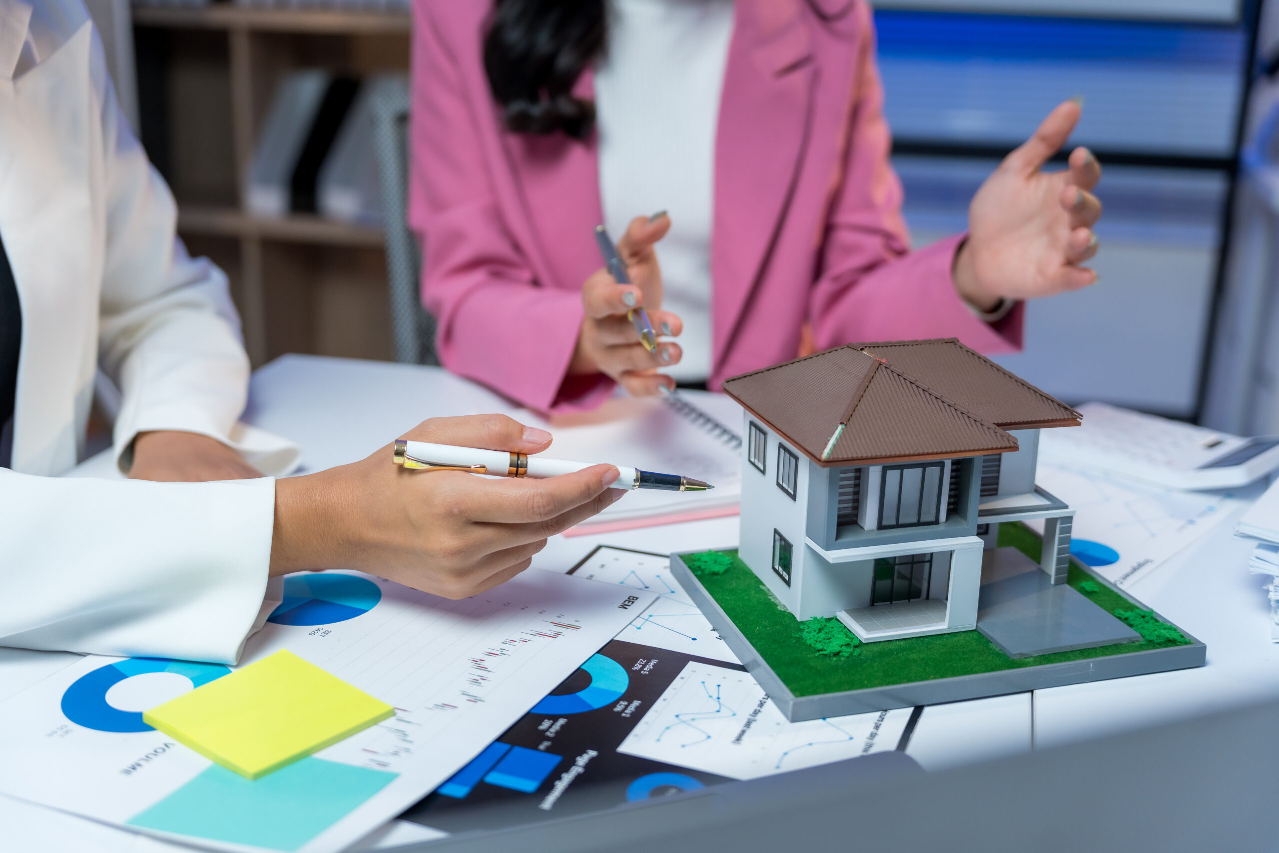Lakáskezelői megbeszélést tartanak egy ingatlanmodell és sok papír fölött